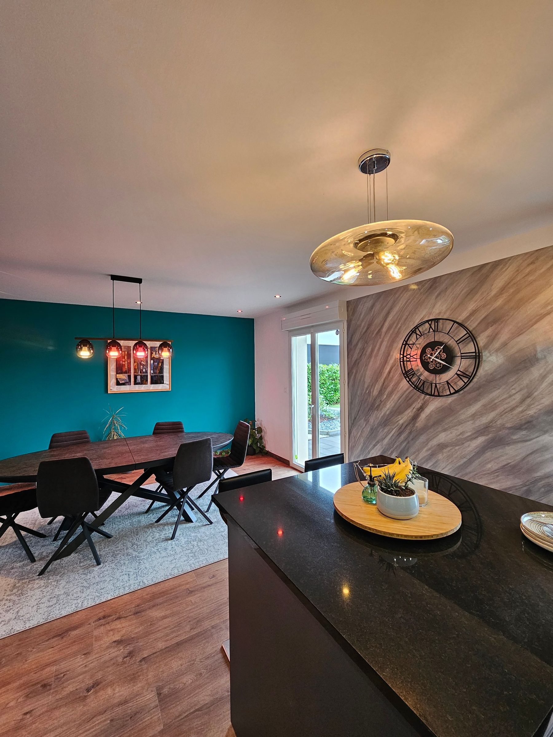 Salle à manger avec mur bleu canard et suspension dorée